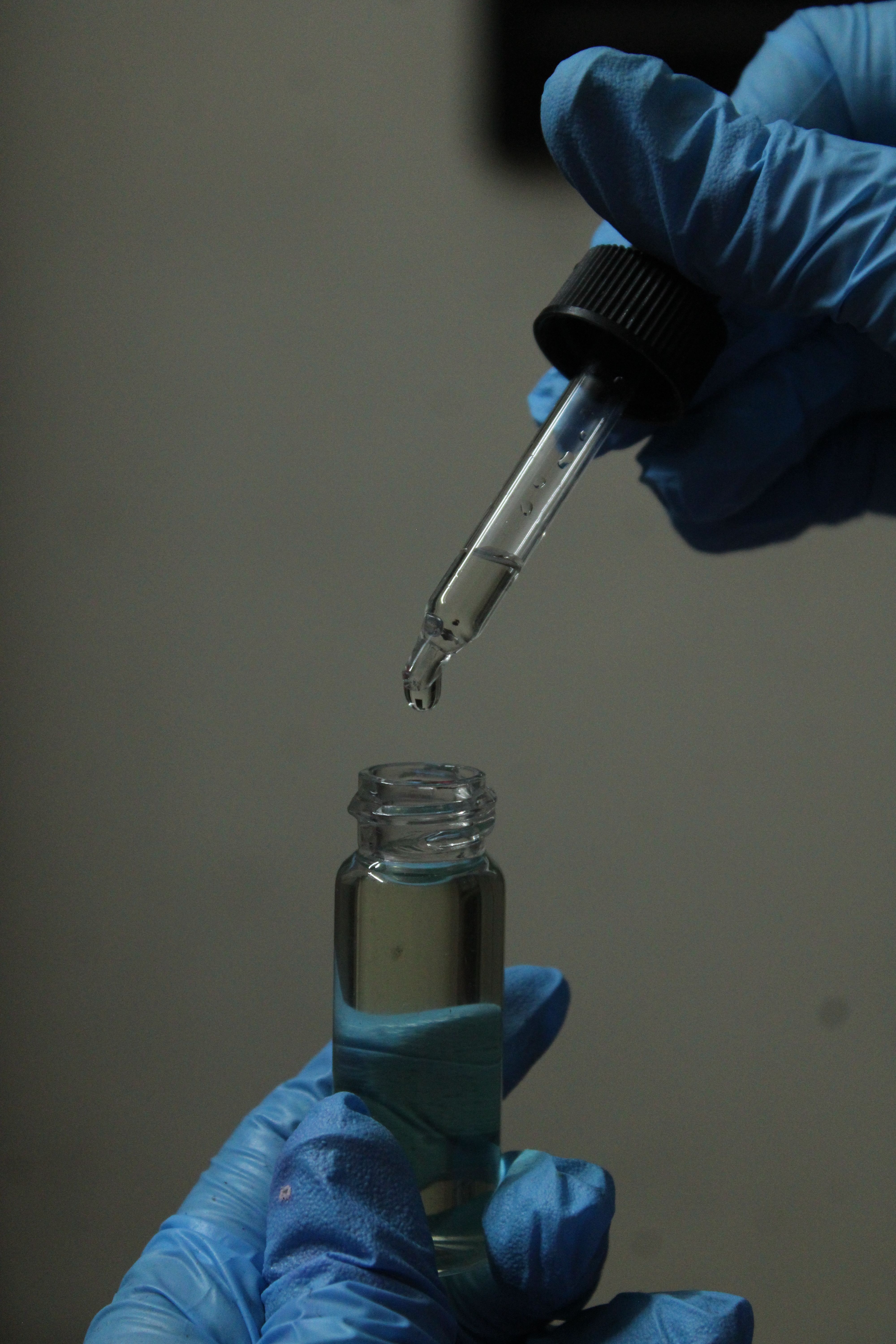 Scientist using dropper to transfer liquid into vial. Laboratory setting.