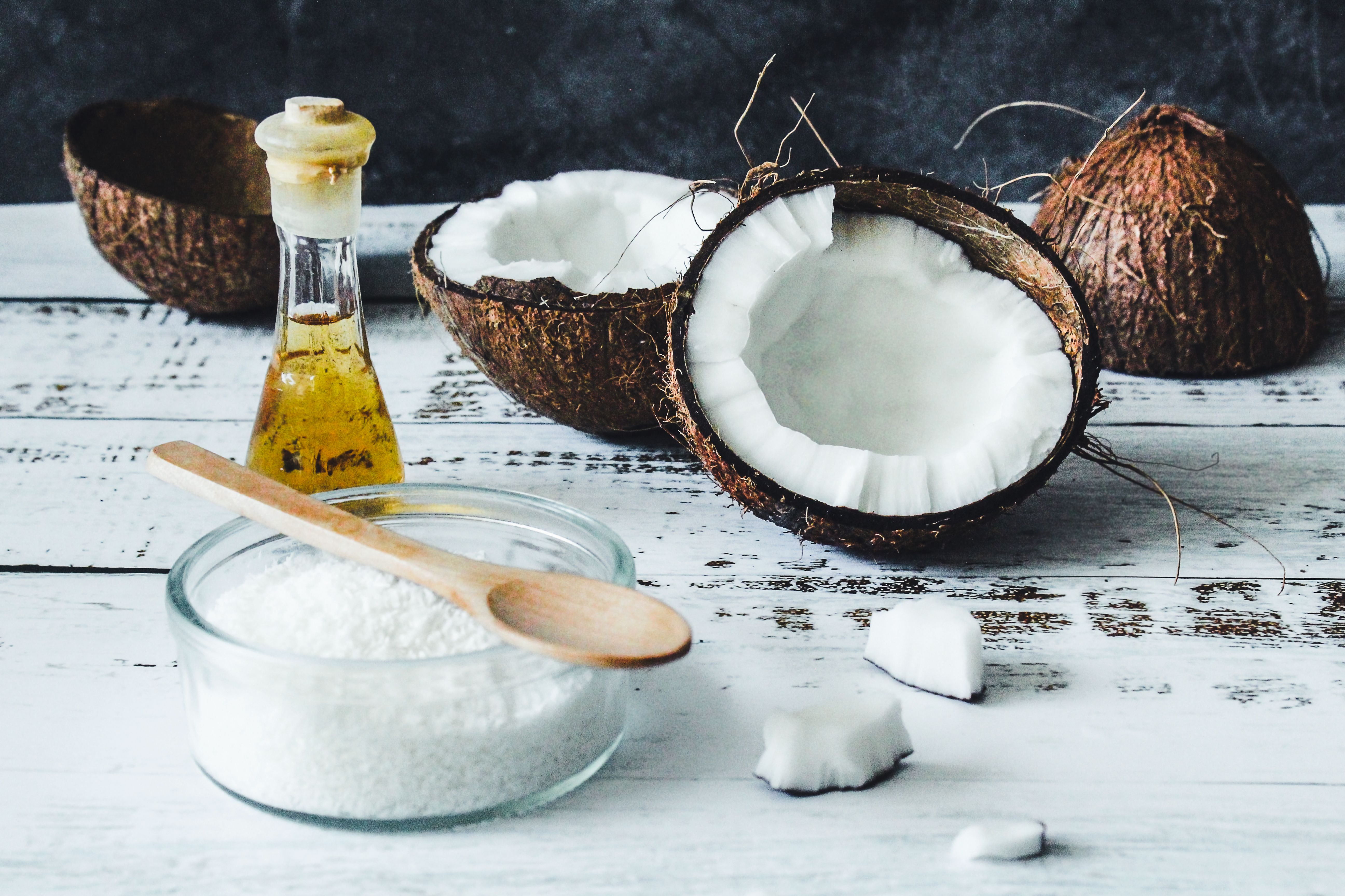Arrangement of coconut oil, flakes, and whole coconuts on a rustic wooden table.